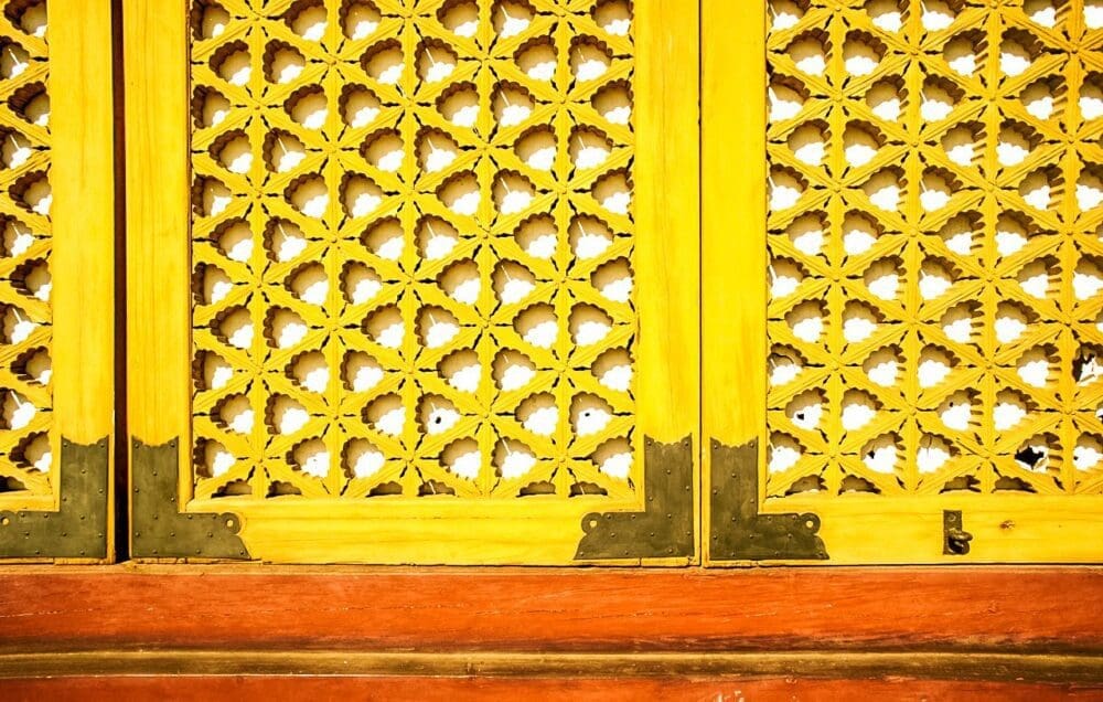 Intricate yellow wood carvings forming a geometric flower pattern on the large exterior doors of a historic palace hall in Seoul.
