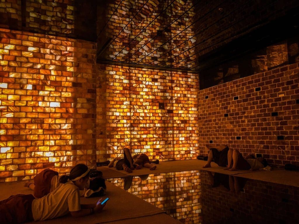 Jjimjilbang 101: Beginner's Guide to Korean Saunas and Bathhouse Etiquette 1 People relaxing on floor mats inside a glowing salt room at a traditional Korean jjimjilbang bathhouse sauna.