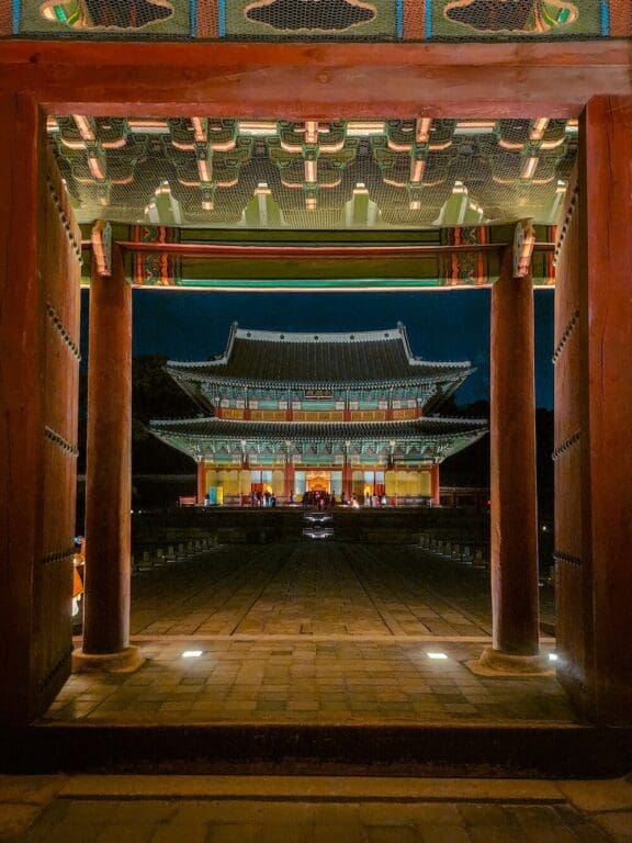 The 5 Royal Palaces in Seoul: A No-Nonsense Expat's Guide to Visiting 8 Injeongjeon Throne Hall lit up at dark, viewed through a gateway during the moonlight tour at Changdeokgung, a highlight among the historic palaces in Seoul.