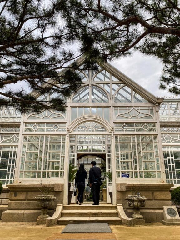 The 5 Royal Palaces in Seoul: A No-Nonsense Expat's Guide to Visiting 9 Visitors walking into the white iron and glass Daeonsil greenhouse at Changgyeonggung Palace, a unique stop among the historic palaces in Seoul.