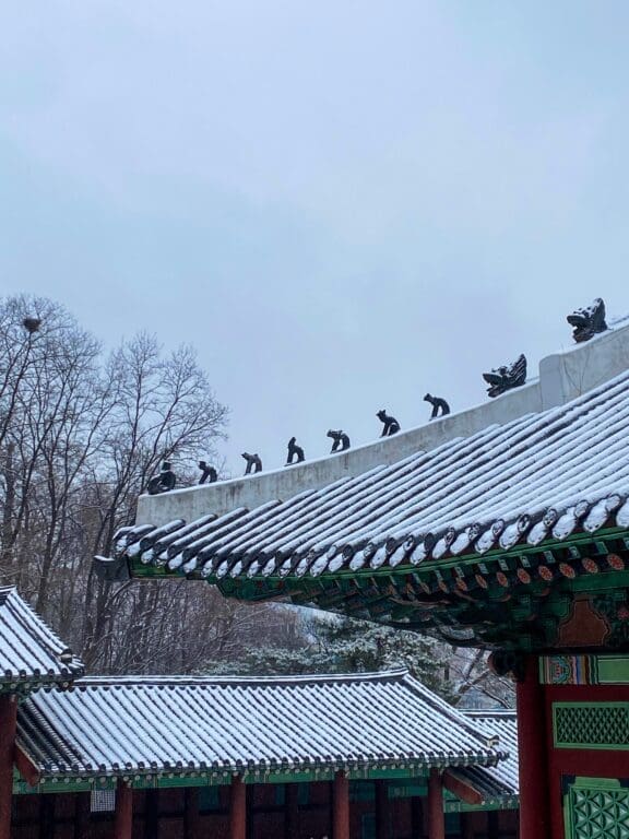 The 5 Royal Palaces in Seoul: A No-Nonsense Expat's Guide to Visiting 14 Traditional tiled roofs covered in snow with decorative Japsang figures at Gyeonghuigung Palace in Seoul.