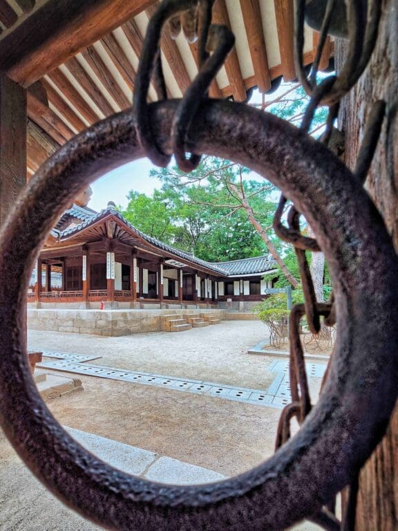 The 5 Royal Palaces in Seoul: A No-Nonsense Expat's Guide to Visiting 15 View of the traditional wooden buildings framed through an old iron door ring at Unhyeongung Royal Residence in Seoul.